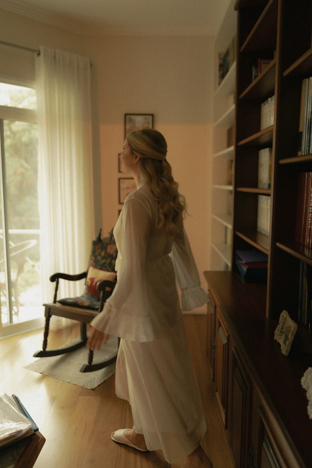 Woman in a white dress walks by a bookshelf